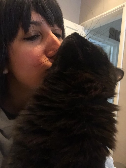a close up of a woman with a black fringe kissing a cat