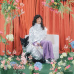 Woman sitting on a chair with a dog, surrounded by flowers