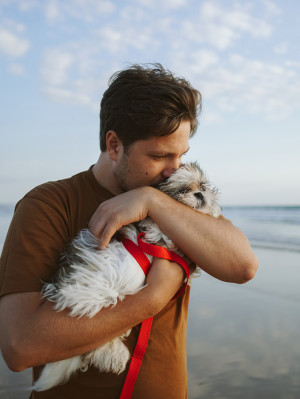 Young man cuddling little white shih tzu puppy by the Atlantic Ocean.
