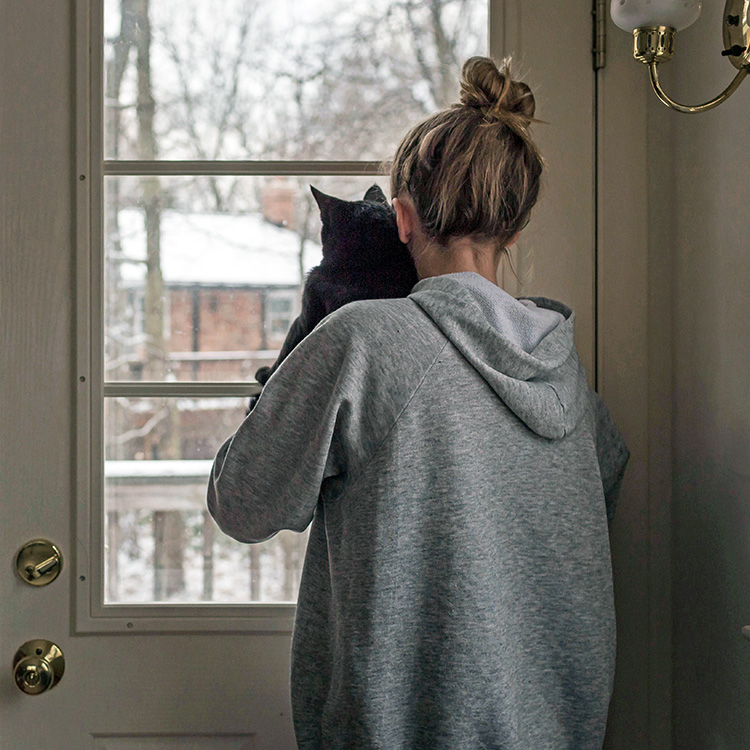 Woman holding her black cat in her arms while looking outside at the snow.
