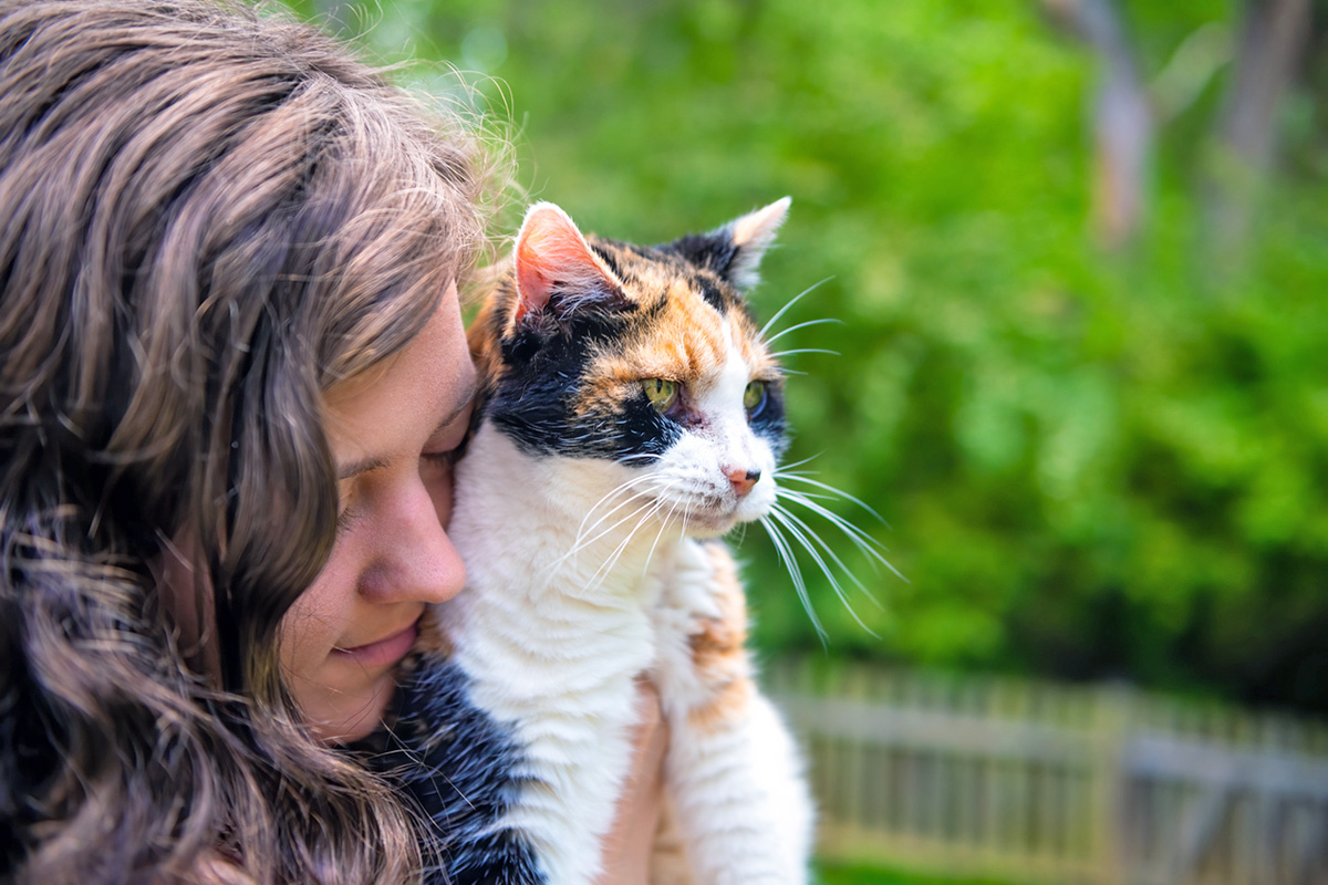 woman with dark hair cuddles calico cat