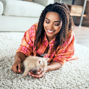 Woman playing with her kitten on the carpet at home.
