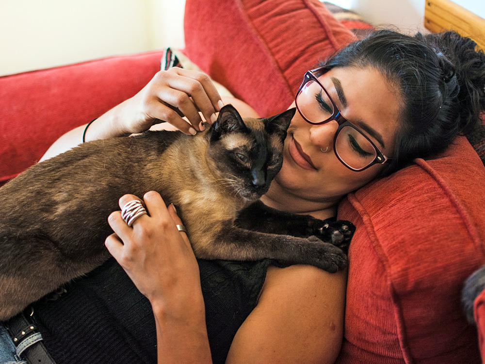 Woman snuggling her Siamese cat at home.