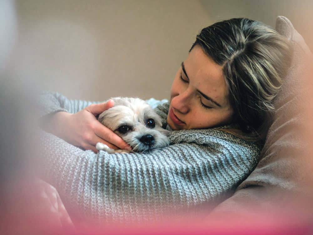 Woman comforting her dog while laying on the couch.