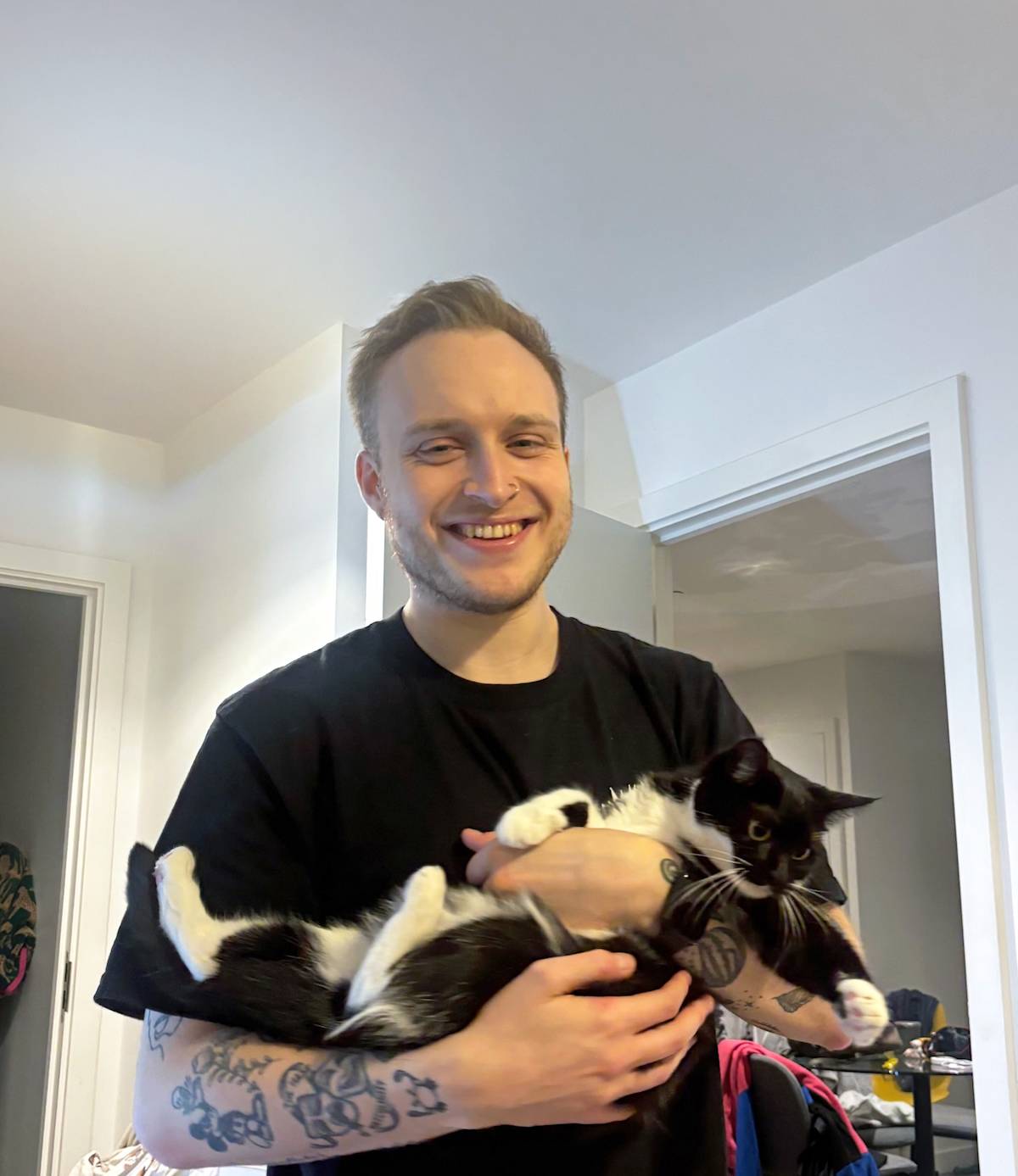 a man with blonde hair and tattoos holding a black and white cat
