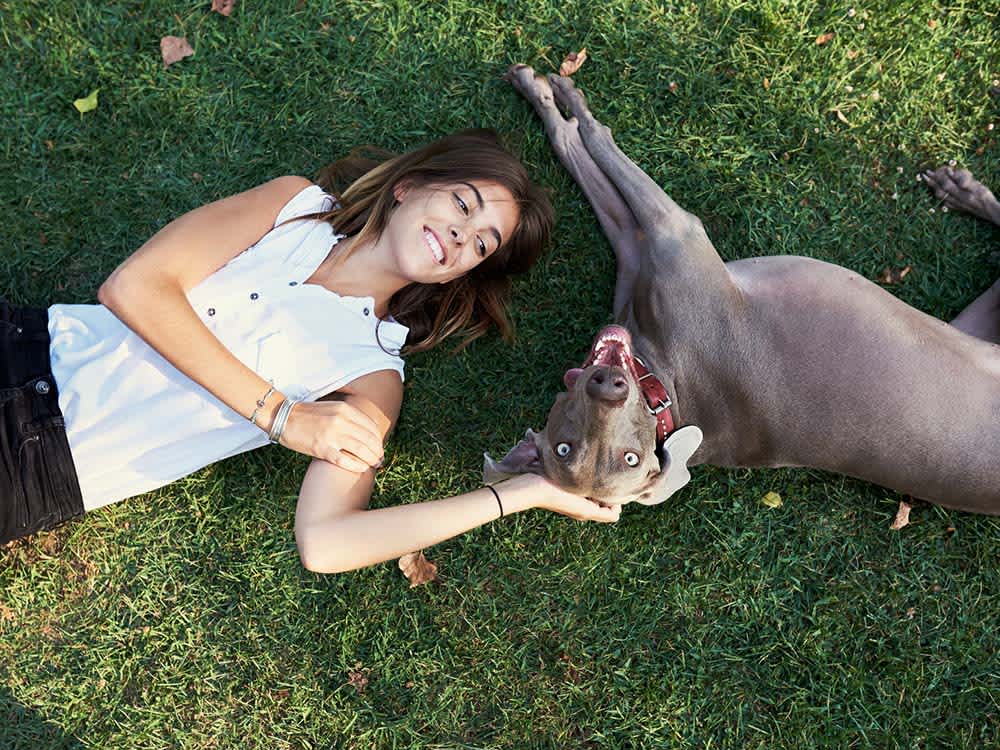 Woman laying on the grass smiling at her dog 