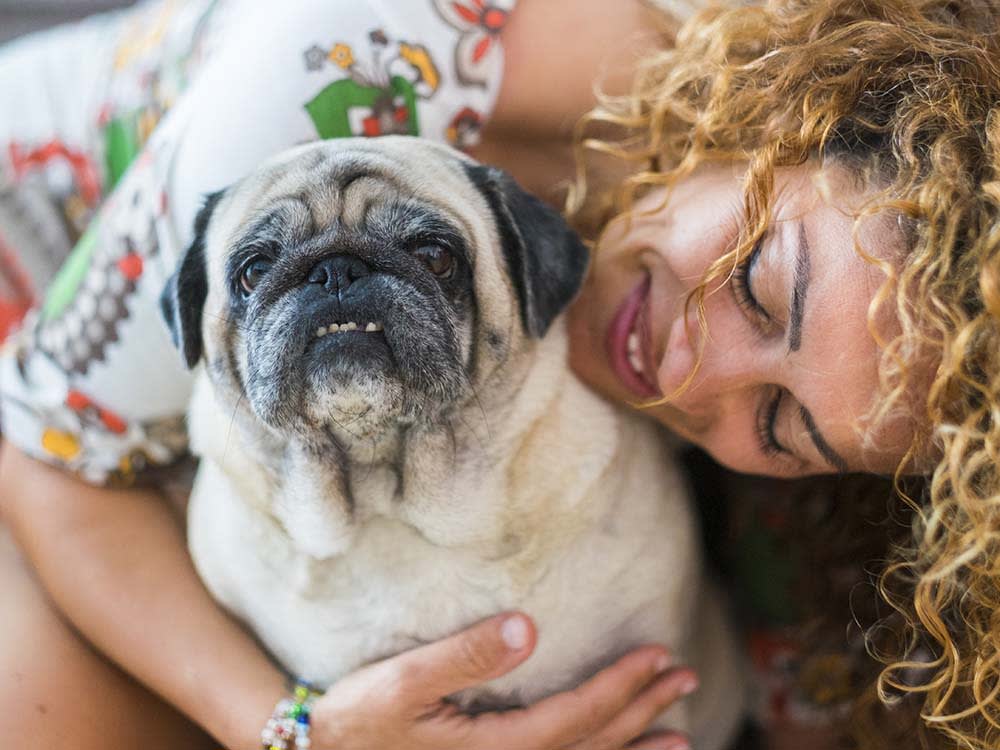 Curly haired blonde woman hugging her old pug dog
