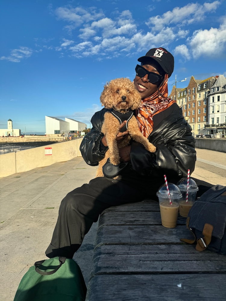 a woman sits on a bench by the beach with a dog