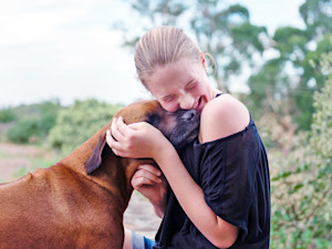Woman hugging her large brown dog outside.
