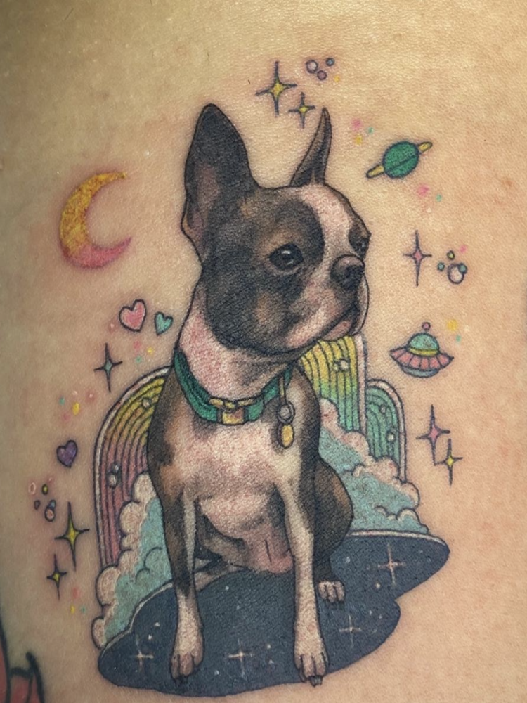 A colour tattoo of a Boston Terrier with rainbows, spaceships and planets surrounding it. 