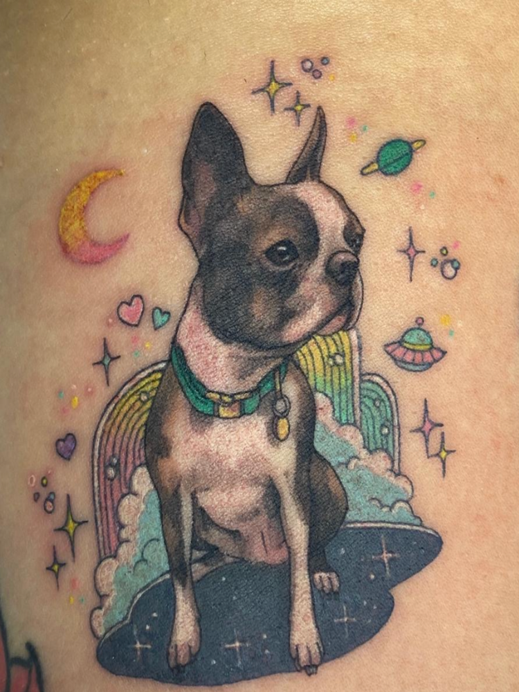 A colour tattoo of a Boston Terrier with rainbows, spaceships and planets surrounding it.
