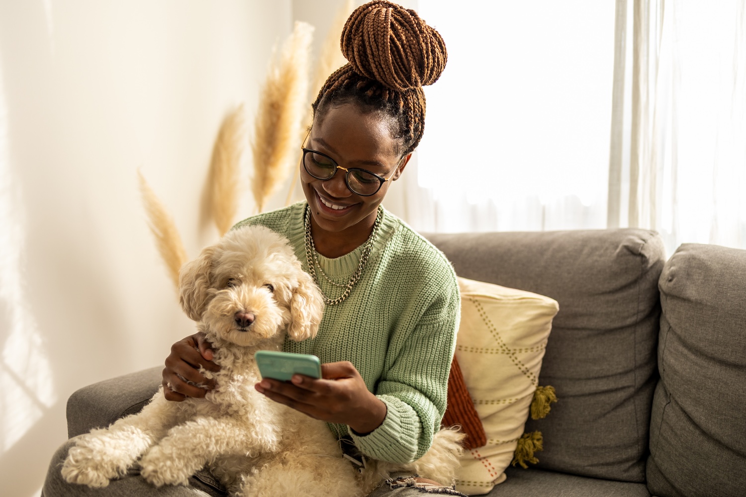 a picture of a girl scrolling on her phone holding a fluffy white dog on her lap