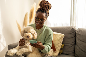 a picture of a girl scrolling on her phone holding a fluffy white dog on her lap