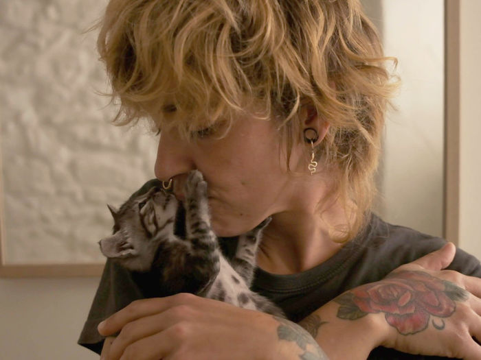 Blonde woman with hand tattoo kissing her gray kitten