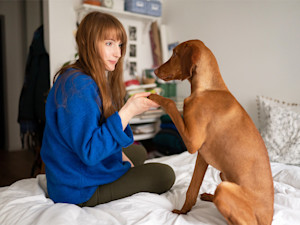 A woman sitting on her bed, holding her dog's paw in her palm.