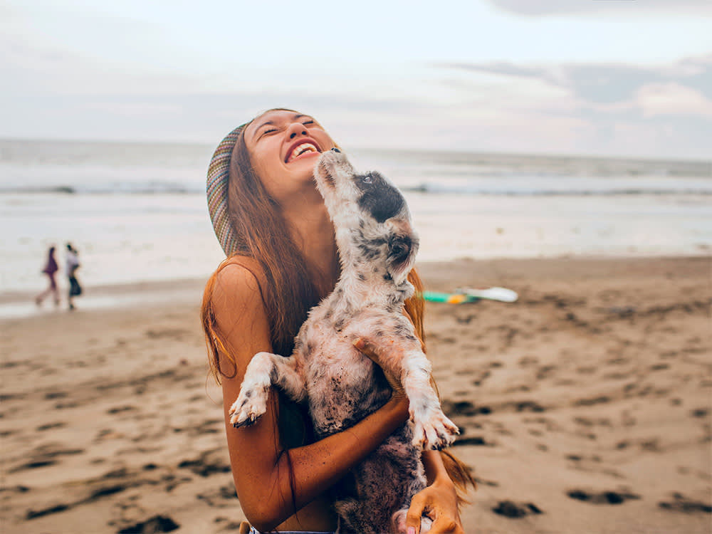 Woman having fun on the beach with her small black and white dog.