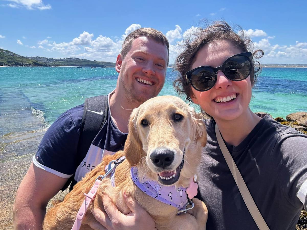 A picture of a man and a woman on a beach holding a golden retriever