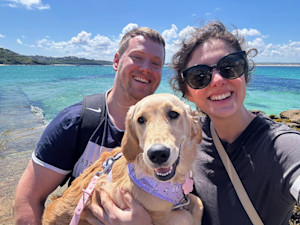 A picture of a man and a woman on a beach holding a golden retriever