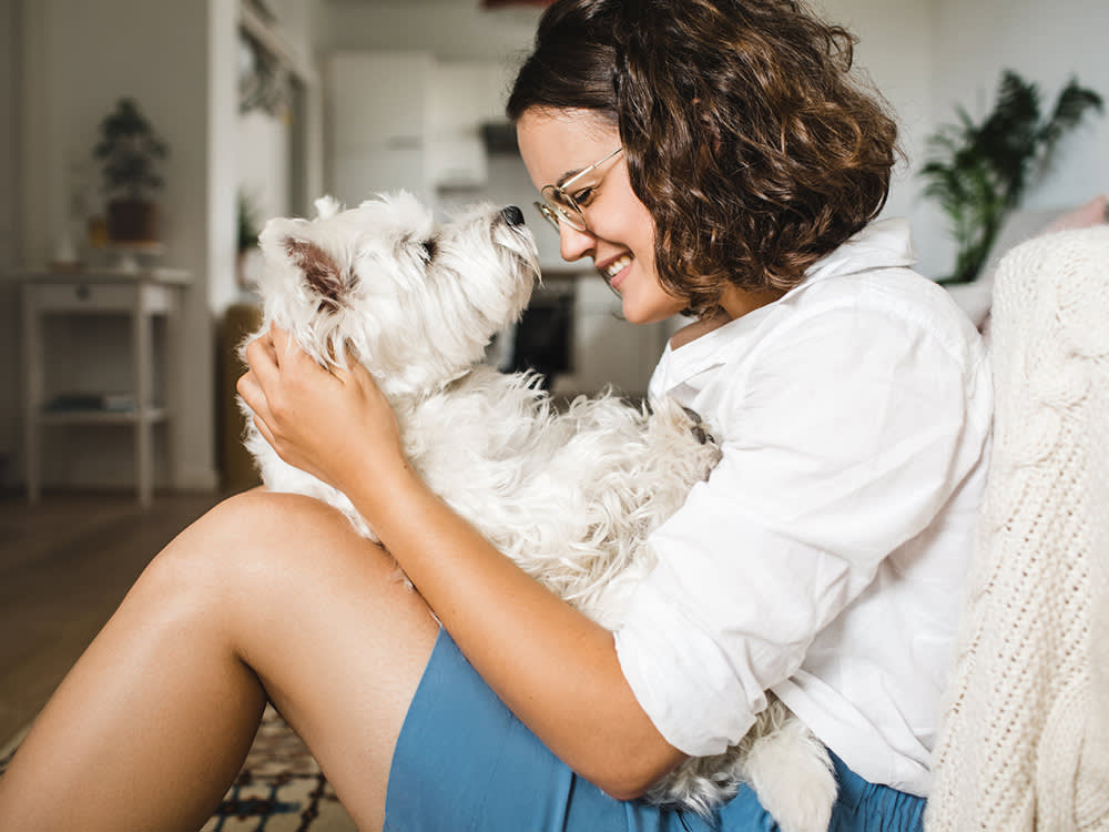 Woman hugging her small white dog at home.