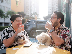 Two guys outside with their small dogs at a cafe.
