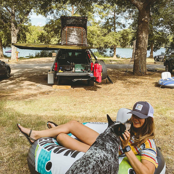 person in innertube petting dog in front of a car with open trunk