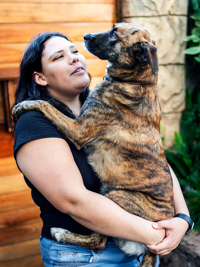 Young woman holding her large dog in her arms outdoors.