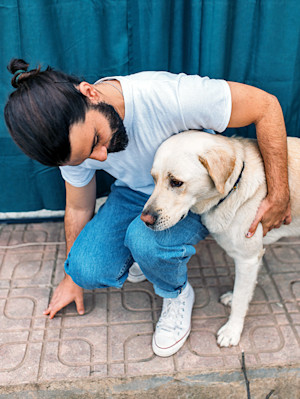 Man comforting his Labrador dog outside.