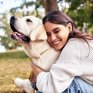 Woman snuggling her senior Labrador dog outside in the grass.
