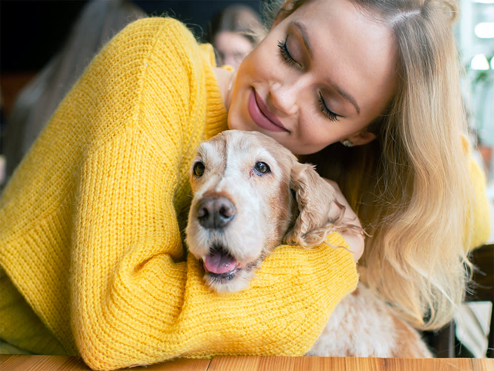 Young caucasian cheerful blonde girl sitting and hugging her lovely cocker spaniel dog in cafe.
