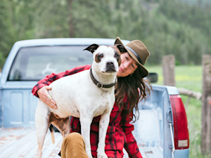 Woman hanging out with her dog in a truck outdoors.