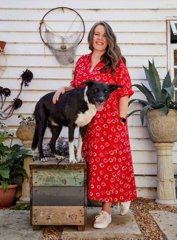 a woman in a red dress stands next to a dog standing on a box