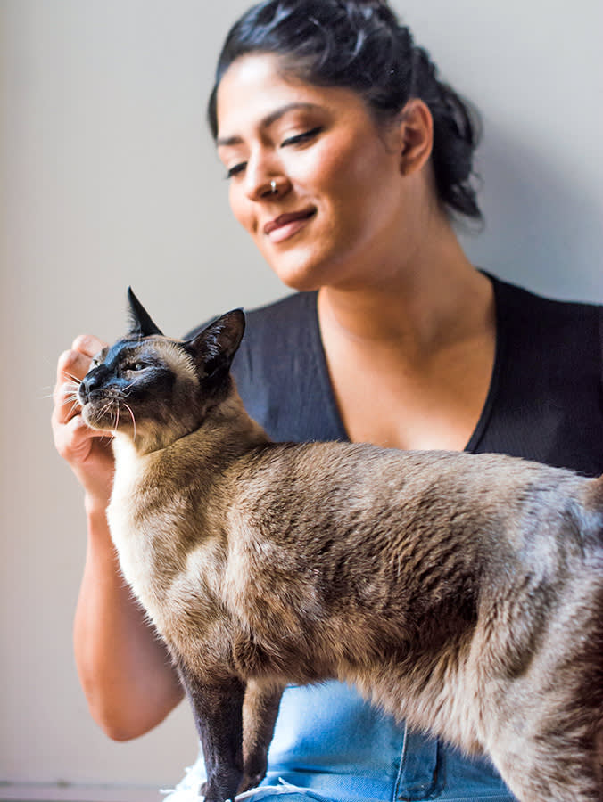 Woman petting her Siamese cat on her lap.