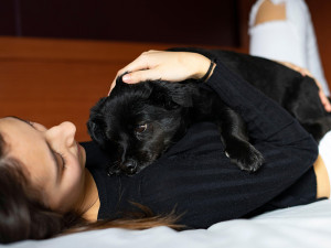 Woman lying in bed hugging a black dog.