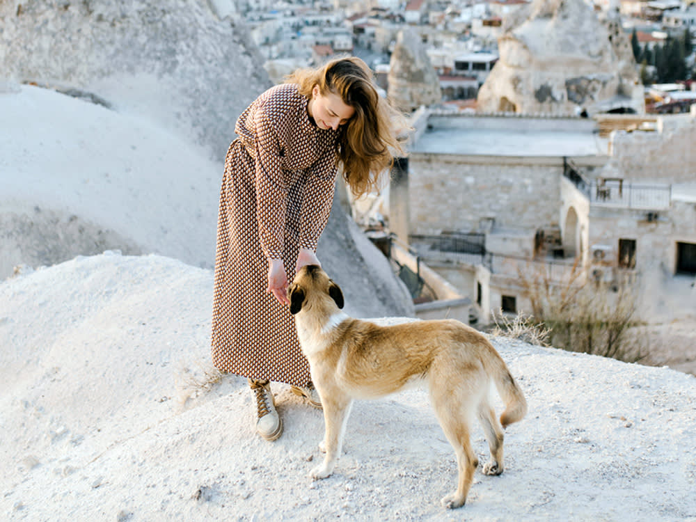 woman on a beach in greece petting a stray dog