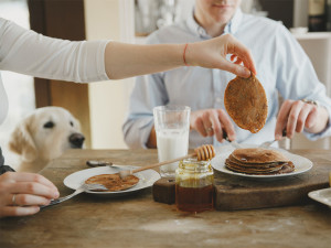 Couple eating pancakes with honey and golden retriever looking at them.