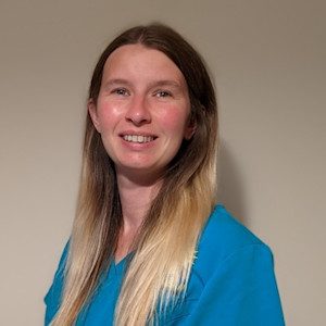 A headshot of a woman with blonde brown hair in blue scrubs