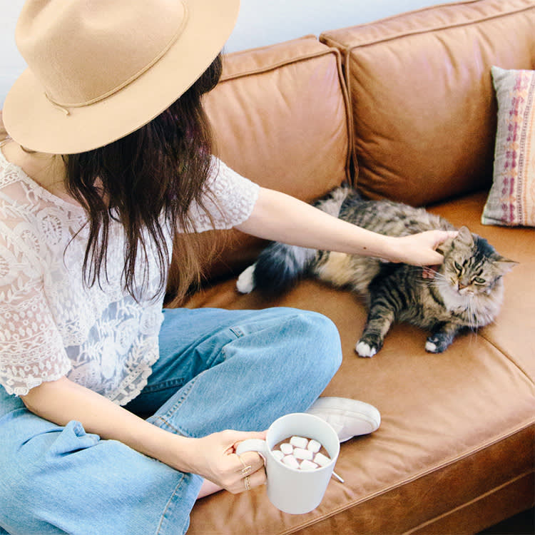 Woman Sitting On Couch Petting Cat, drinking hot cocoa with marshmallows.
