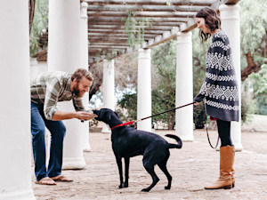 Man petting a black dog on a leash outside.