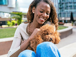 Woman holding her small brown doodle dog outside.
