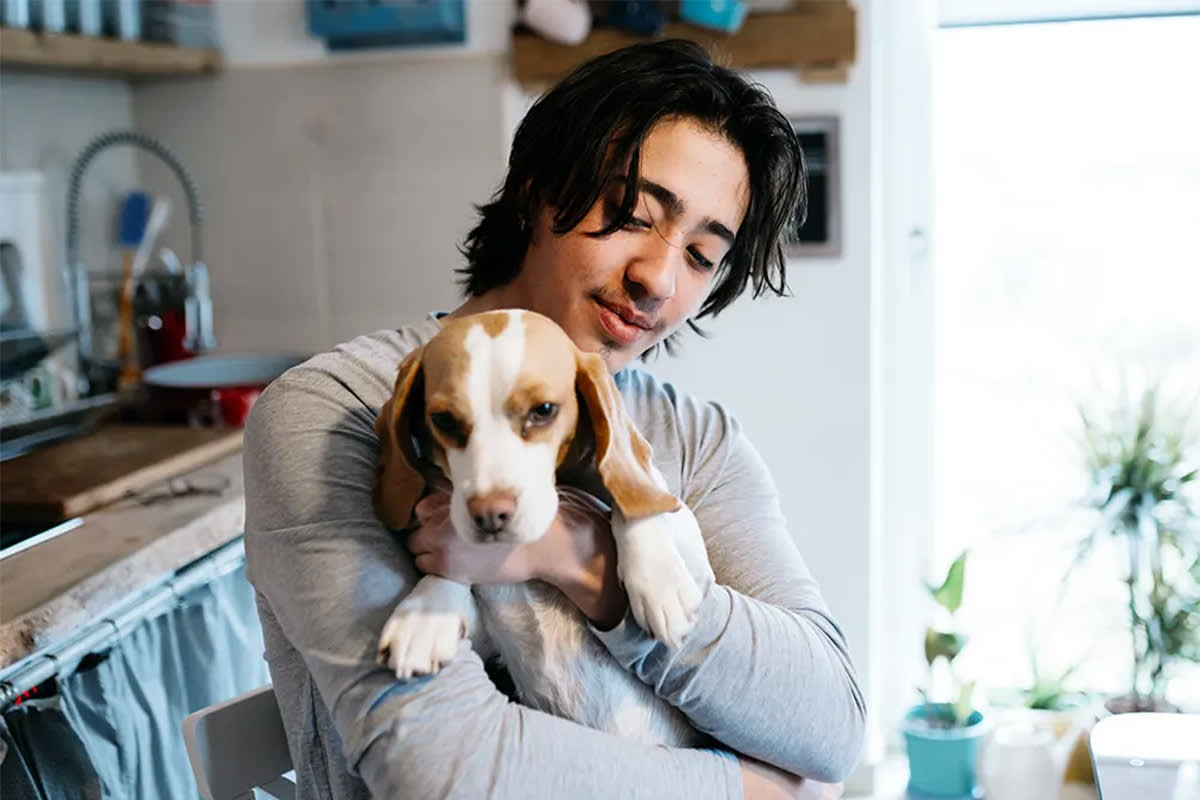 A man holds a dog while standing in a kitchen.