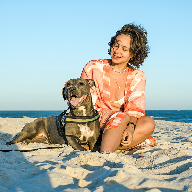 Woman on the beach with her Pit Bull dog.