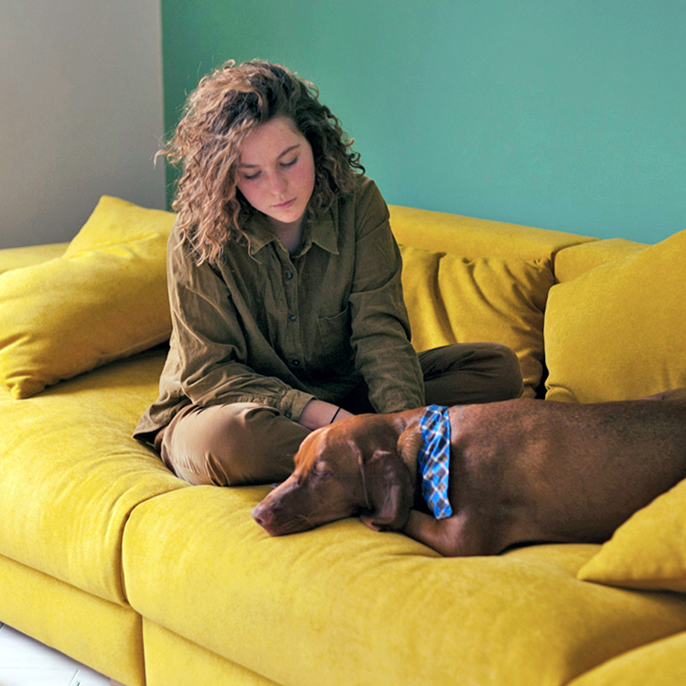 Girl sits on the couch and looks at the sleeping dog.