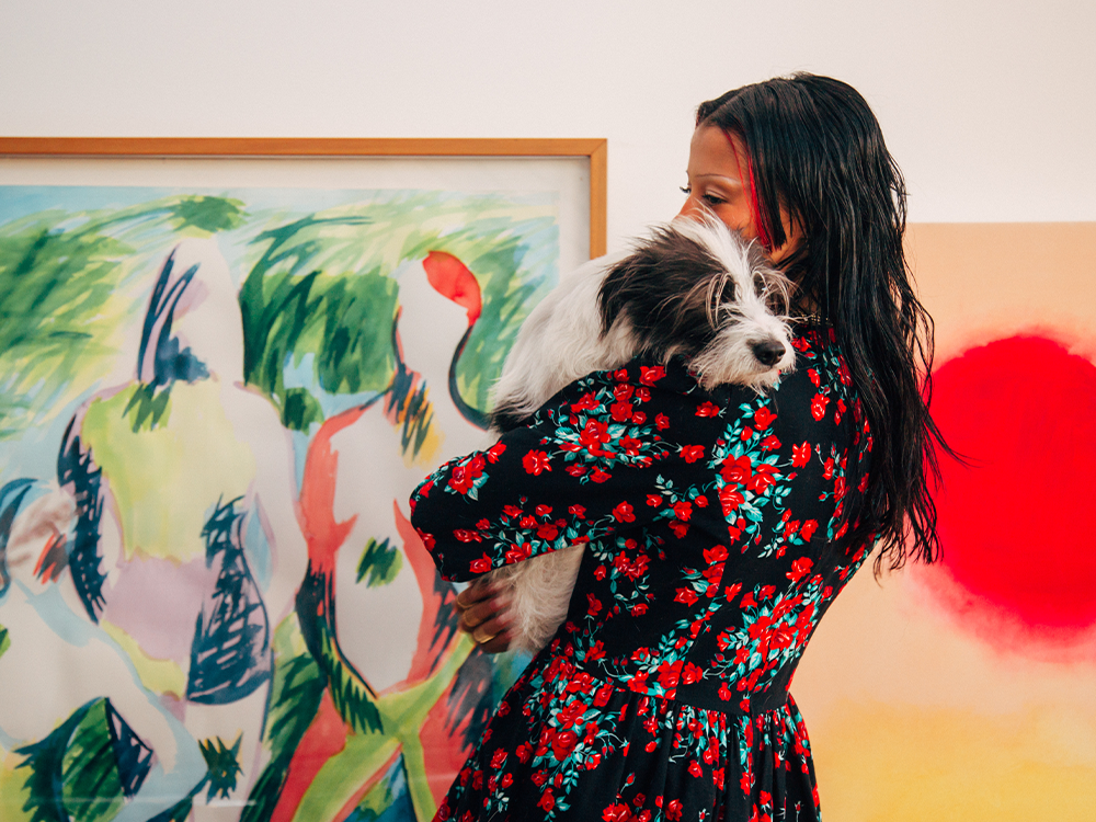 Sami Miró holding her small rescue dog in front of two colorful abstract art pieces