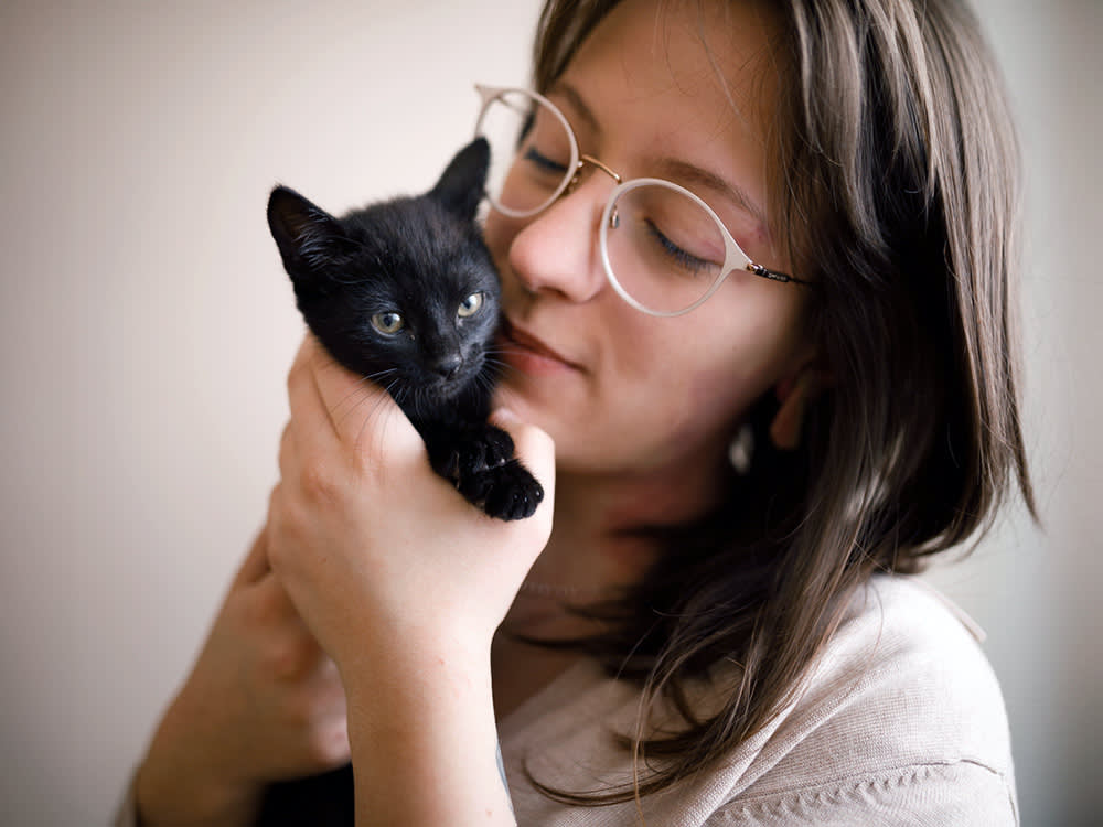 Relaxed girl holding a black kitten near her face.