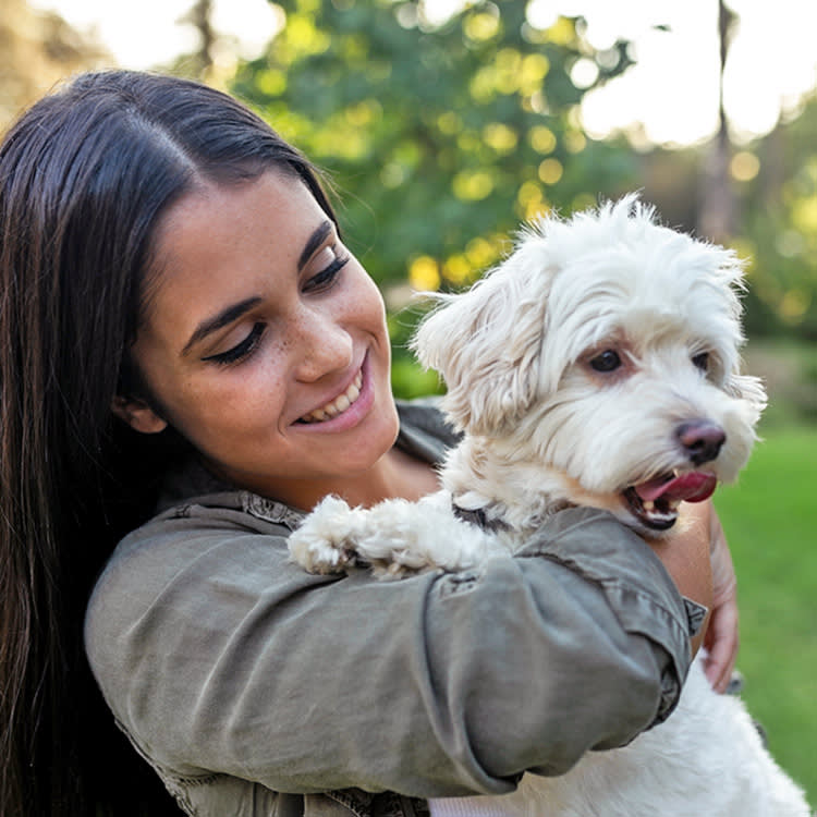 College woman holding her small white fluffy dog.