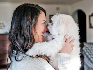 Happy woman holding her small white dog at home.