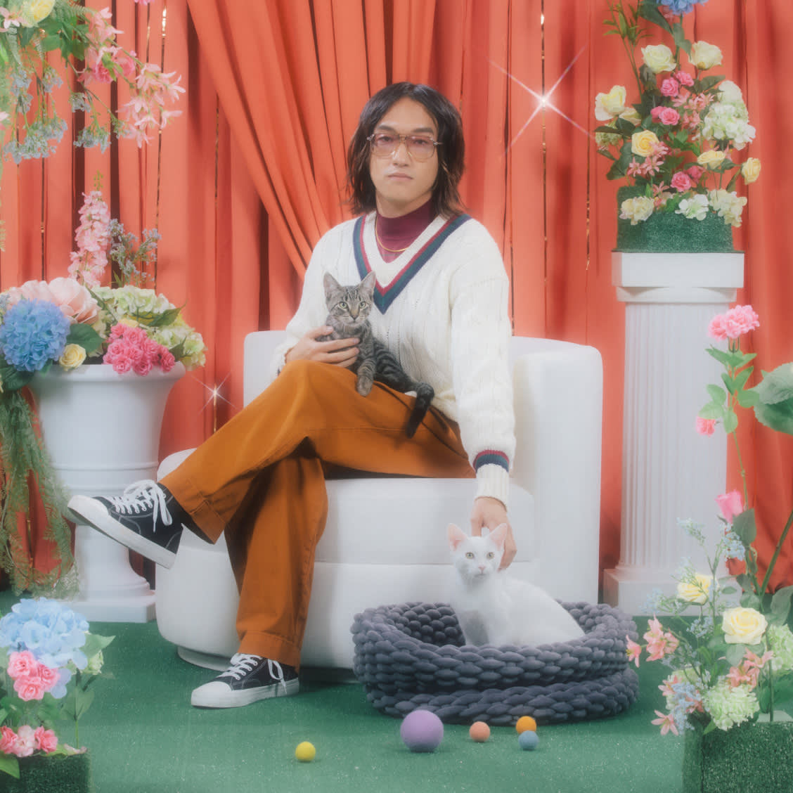 Man sitting with cats, surrounded by flowers