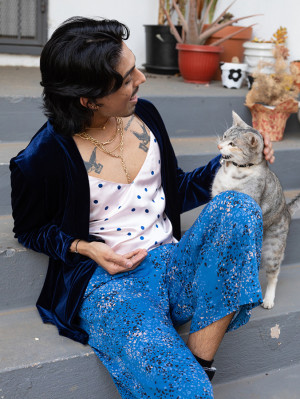 Happy stylish latino queer person looking comfortable on porch steps with gray cat.