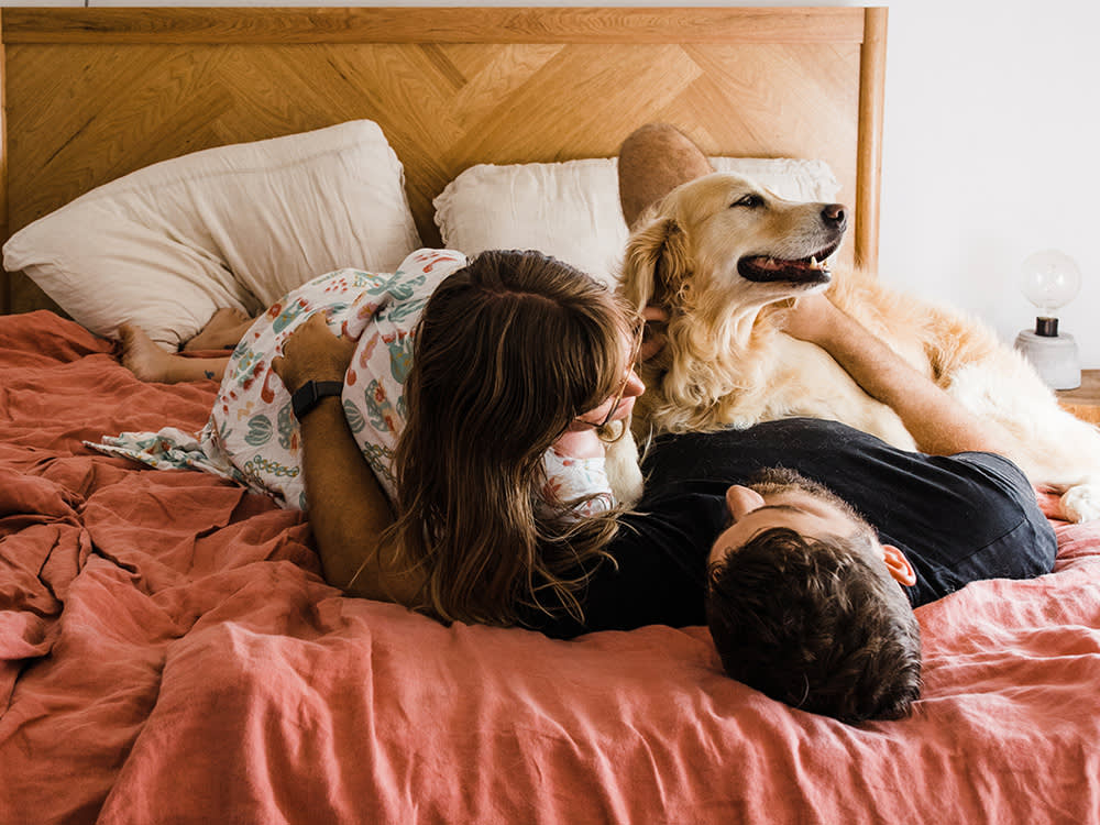 A couple laying on a bed with their golden retriever. 