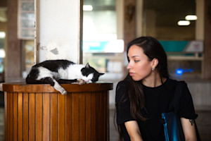 a picture of a dark haired young woman looking at a sleeping black and white cat